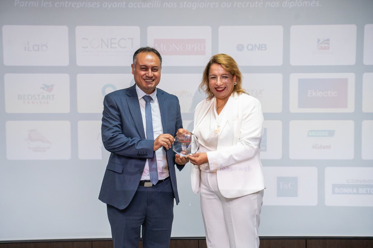 Remise d'un trophée Manager 4.0 devant le mur des entreprises partenaires